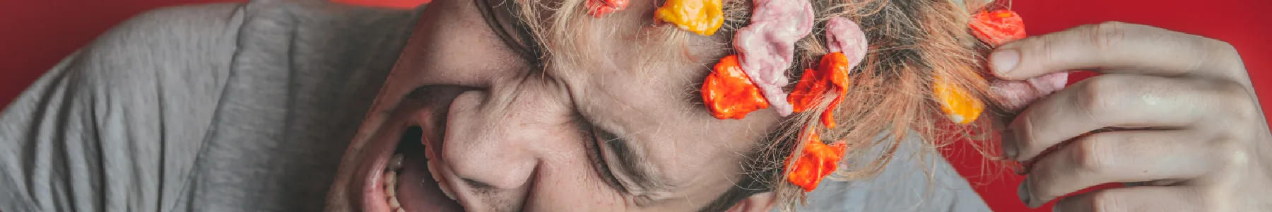 Obrázek nešťastného muže kroutící se v bolestech s barevnými žvýkačkami ve vlasech vyjadřující kontroverzní přísady běžně dostupných žvýkaček | Pro web: zdravezvykani.cz | Zdroj: shutterstock.com