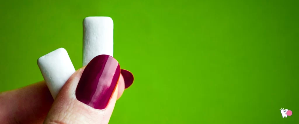 Weißer Kaugummi in den Fingern einer Frau mit lackierten Nägeln auf grünem Hintergrund | Quelle: Shutterstock | Für den Artikel: Definition von Kaugummi | Für die Website: gesunderkaugummi.de