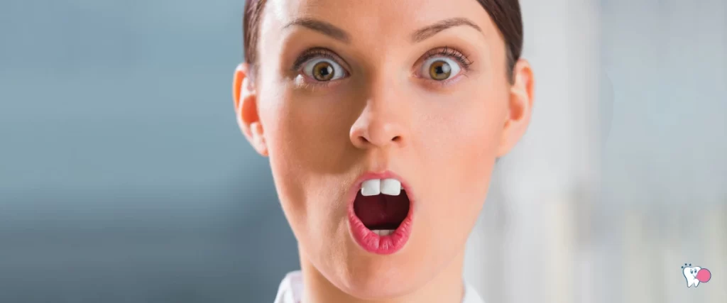 Ein Foto einer Frau mit offenem Mund und hervorgehobenen Zähnen in Kaugummigröße mit grauem Hintergrund | Quelle: Shutterstock | Artikel: Wahr oder fake? | Kaugummi in den USA erfunden? | Website: gesunderkaugummi.de